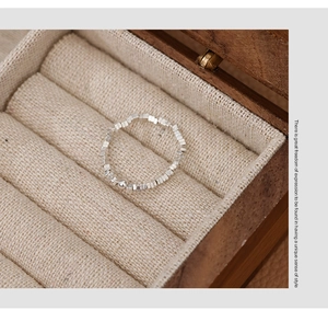 Macro shot of silver beaded ring with square beads on a beige linen jewelry box liner