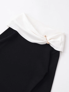 Detail of contrast stitch knit top featuring black ribbed fabric and golden pin fastener