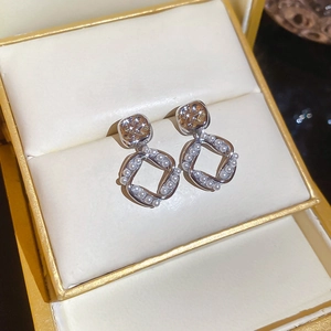 Macro view of silver-tone earrings with brown square stud and twisted pearl pendant