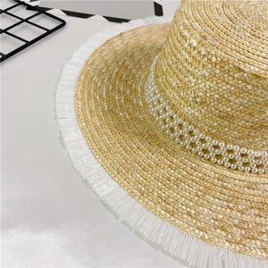 Detailed macro view of straw hat featuring triple-row pearl band and white fringe edges