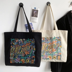 Detail of embroidered canvas tote bags in black and beige hanging on a white wall