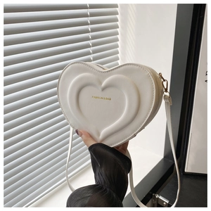 Macro detail of white heart-shaped crossbody bag with embossed layers and gold hardware