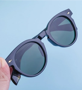 Detail shot of black oval sunglasses featuring signature gold arrow hinge accents