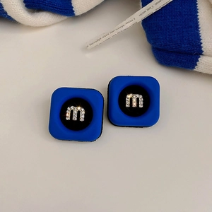 Detail of Klein blue square stud earring with rhinestone M motif on white background