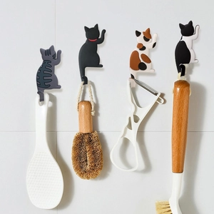 Set of four cartoon cat tail magnetic fridge hooks holding kitchen utensils on tiles