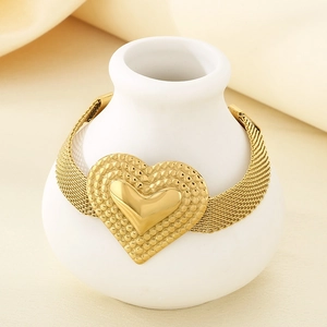 Goldenes Gliederarmband mit strukturiertem Herzanhänger auf weißer Vase