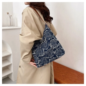 Detail of blue denim tote bag with white floral embroidery and brown leather strap