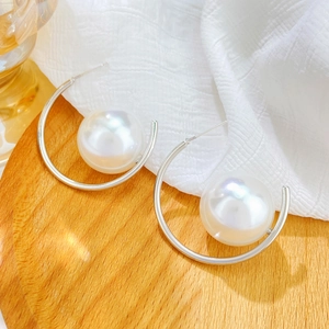 Detailed view of silver C-shaped earrings with large white pearls on a textured background