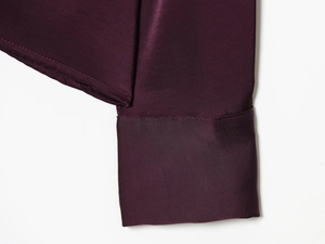 Détail du poignet d'une chemise en satin violet foncé avec texture soyeuse et coutures