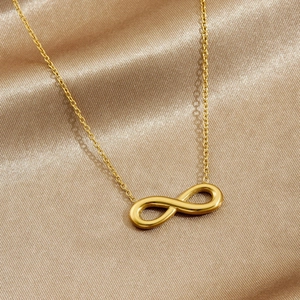 Minimalist gold-plated stainless steel infinity pendant necklace on elegant silk background