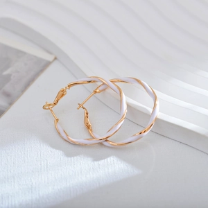 Detail view of gold metal and white oil drip hoop earrings on a textured background