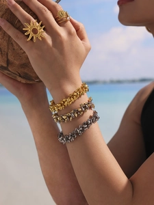Detail of sun-shaped ring and layered spiked bracelets on a model at the beach