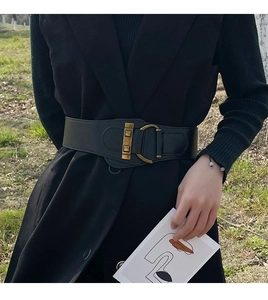 Detail of a wide black elastic waist belt with a vintage gold metal buckle on a black suit