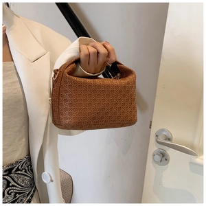 Detail of woven brown handbag featuring gold hardware held by a woman in a white blazer