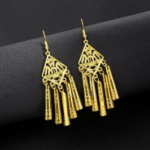 Detail of golden ethnic earrings with diamond-shaped hollow frame and textured drop on leather