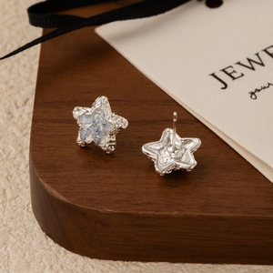 Elegant star-shaped silver stud earrings with light blue crystals on a wooden display