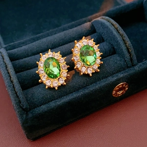Macro shot of green oval gemstone earrings with white zircon halo in a navy velvet box