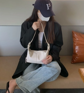 Chic cream white faux leather shoulder bag with gold hardware worn in a stylish setting