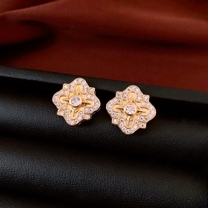 Macro shot of gold-plated flower earrings with white zircons on black leather and red silk