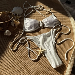 Flachbild von weißem glänzendem Bikini mit Goldring-Detail auf einer gewebten Strandmatte