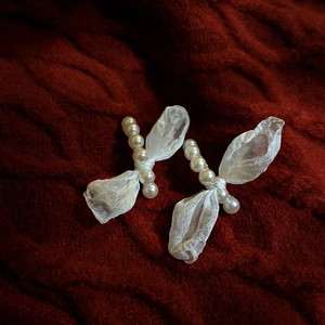 Macro shot of white pearl bow earrings with translucent tulle on red knit background