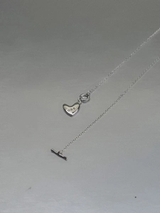 Macro detail of silver heart pendant necklace with minimalist toggle clasp and fine chain