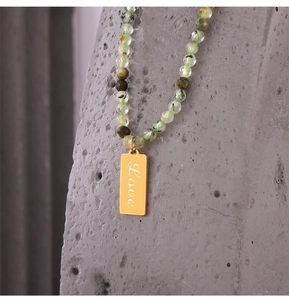 Macro shot of gold pendant engraved with Love on a green peridot beaded necklace