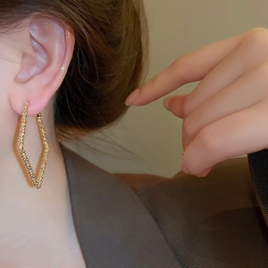 Detailed close-up of textured gold geometric rhombus earrings on a model’s ear