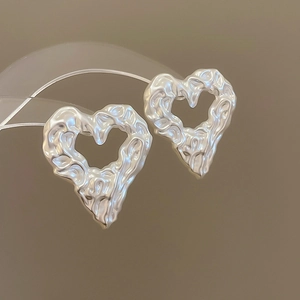Detail of silver heart earrings with irregular hammered metal texture on arch stand