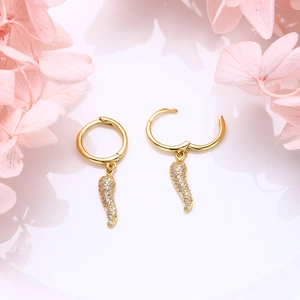 Detail of gold-tone feather pendant earrings with white cubic zirconia on floral background