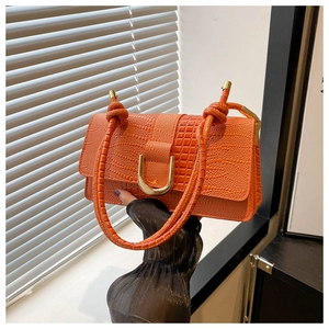 Detail of orange crocodile pattern handbag featuring a gold horseshoe buckle and textured handle