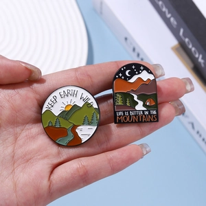 Outdoor themed enamel pins featuring mountains and desert tents held by a model