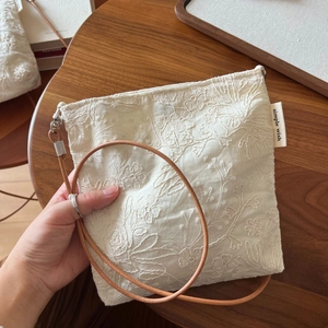 Detail of floral embroidery on beige linen crossbody phone bag with slim leather strap