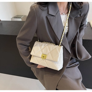 Detail of white quilted crossbody bag with gold chain strap worn by a model in a blazer