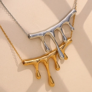 Detail view of liquid metal pendants in gold and silver finishes on beige background