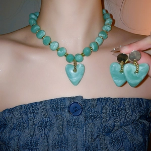 Detail of mint green heart pendant necklace and matching earrings on a female model