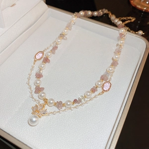 Detail of double-layer necklace with pink stones, pearls and golden crown pendant