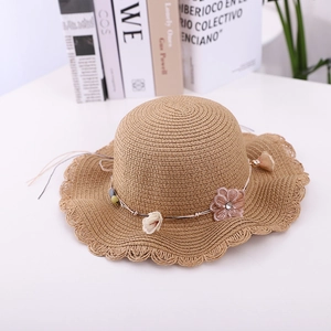 Detailed view of a light brown woven straw hat with lace flower decor on white desk