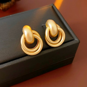 Detail of interlocking matte gold hoop earrings with a frosted texture on a jewelry box