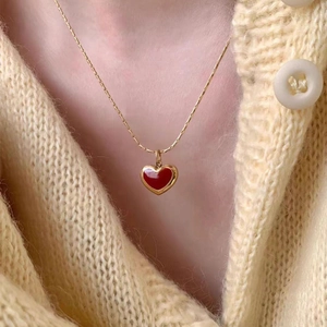Detail of red heart pendant necklace on golden chain worn with yellow sweater