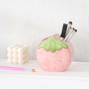Cute pink ceramic strawberry pencil holder and makeup brush organizer on a desk