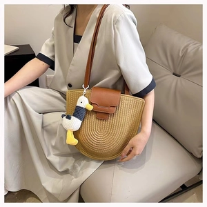 Detail of light brown woven straw bag with leather strap and cute plush duck charm accessory