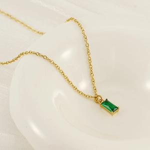 Elegante collana dorata con pendente verde smeraldo presentata su un piatto ceramica