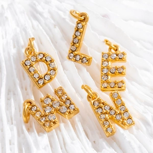 Macro shot of gold-plated D, L, E, W, N letter pendants with white zircon inlay on white coral