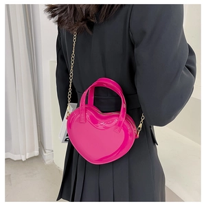 Detail of a bright pink heart-shaped jelly bag with a gold chain strap worn by a model