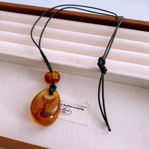 Macro shot of amber resin drop pendant with black cord in a beige jewelry box
