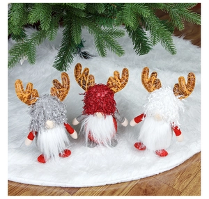 Three plush Christmas reindeer gnomes with knitted hats on white faux fur tree skirt
