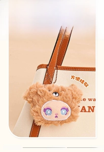 Close-up of a brown plush cartoon bear keychain charm attached to a canvas bag