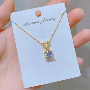 Detailed macro view of a gold-toned necklace with a square-cut zircon stone on a white card