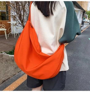 Close-up of a large orange crescent-shaped oxford cloth crossbody bag on a model